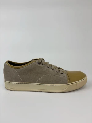 Beige Lanvin sneakers med mocka och lackdetalj - Snygga beige sneakers med ovandel i mocka och glansig lackad tå i ljusbrunt. Skorna har beige snörning och en krämfärgad sula. Perfekta för dig som gillar stilrena och unika detaljer på dina sneakers.