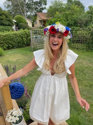 Vit kort klänning med volangärmar - Superfin vit kort klänning med volangärmar och djup v-ringning. Klänningen har öppen rygg med knyt och är perfekt för sommarens alla tillfällen. Tillverkad i ett lätt och luftigt material som känns bekvämt hela dagen, perfekt till studenten!