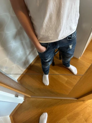 Mörkblå slitna jeans med relaxed fit - Säljer ett par mörkblå jeans med relaxed fit och snygga slitningar på låret. Jeansen har klassisk femficksdesign och en något lösare passform. Perfekta för en avslappnad och trendig stil.