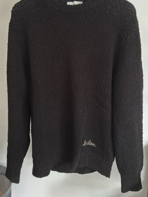 Svart stickad tröja från Les Deux - Mysig svart stickad tröja från Les Deux med broderad logga nertill. Tröjan har rund halsringning, lång ärm och ribbstickade muddar. Perfekt för kyligare sommardagar och enkel att matcha med andra plagg. Skick: 9/10