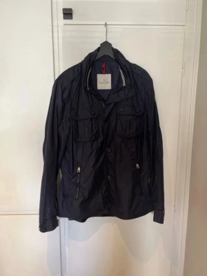 Marinblå Moncler Field Jacket (Storlek M) - En väldigt snygg Moncler ”Mate” Field Jacket i fint skick! Den är storlek 4, sitter som en storlek M. Skriv om det finns några funderingar😁
