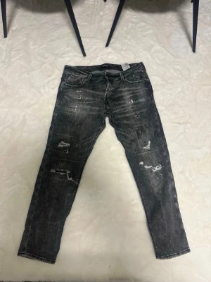 Svarta Jeans från Jack & Jones - Säljer ett par svarta jeans med slim fit och slitna detaljer samt färgstänk på benen. Jeansen är från Jack & Jones och perfekta för en trendig och avslappnad streetstil.