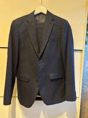  mörkblå kostym i slim fit + skjorta (använd 1 gång) - Säljer en kostym i mycket fint skick, endast använd 1 gång. Inkluderar, kavaj, byxor, skjorta. Nypris 2699 och säljes för 995. Storlek 44 på Kavaj och byxor. Skjorta storlek S. Märke Riley. Tveka inte att höra av er vid frågor! Kan skicka exakta mått om det behövs!