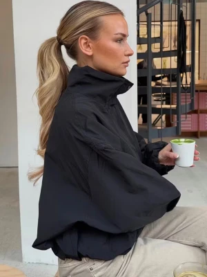 Svart oversized vindjacka med hög krage - Stilren svart vindjacka i oversized modell med hög krage och dolda fickor. Jackan har en minimalistisk design och är tillverkad i lätt, vindtätt material som passar perfekt till streetwear-looken. Dragkedja framtill och breda ärmar för en avslappnad vibe.