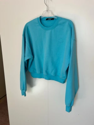 Turkos sweatshirt från BikBok – Stl XS - Säljer en jättefin turkosblå sweatshirt i croppad modell från Bik Bok. Tröjan har en diskret, broderad logotyp på bröstet ("BB Sport") i matchande färg. Perfekt till ett par jeans eller mjukisbyxor med hög midja!  • Material: Mjuk bomullsblandning (74% bomull, 26% polyester) • Skick: Sparsamt använd och i fint skick.  •Rökfritt hem •Djurfritt hem • Köp gärna som bundle (paketpris) för att spara på frakten! Jag har fler liknande plagg ute nu.