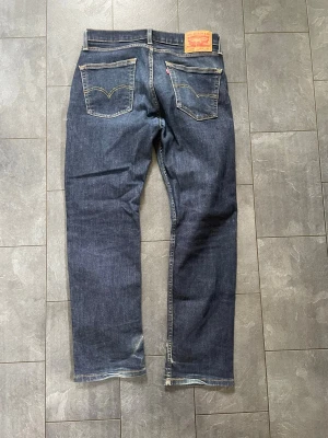 Levi's 514 raka jeans mörkblå - Mörkblå raka jeans från Levi's modell 514 med klassiska bakfickor och kontrastsömmar. Jeansen har en tydlig läderpatch bak i midjan och är tillverkade i slitstark denim. Perfekta för en avslappnad och stilren look.