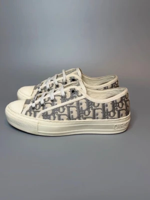 Dior sneakers  - Snygga låga sneakers från Dior med klassiskt grått och vitt Oblique-mönster. Skorna har vita snören, gummisula och tydlig Dior-logga på sidan av sulan. Tillverkade i canvasmaterial med detaljer i gummi. Perfekta för dig som gillar exklusiv streetstyle.