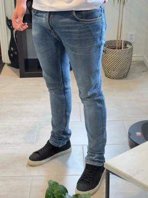 Nudie Jeans Tilted Tor blå jeans W33/L32 - Snygga blå jeans från Nudie Jeans i modellen Tilted Tor. Slim/tapered passform med stretch för bekväm fit. Tvätt i “True Cold Blue” och tillverkade i 99% organic cotton. Storlek W33/L32. Bra skick och passar perfekt till både vardag och streetwear.  Modellen på bilden är ca 185 cm lång och väger ca 78 kg för referens.