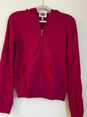 Kashmir hoodie från Juicy Couture - Snygg ceriserosa hoodie från Juicy Couture med dragkedja i guld, huva och två fickor framtill. Tillverkad i mjukt stickat material som känns skönt mot huden. Perfekt för en avslappnad och trendig look. Storlek XL men passar mig som har S/XS.