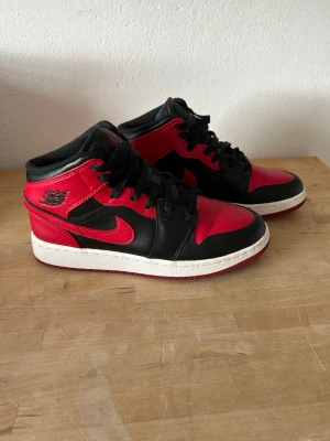 Air Jordan 1 Mid Bred Svart/Röd - Säljer ett par Air Jordan 1 Mid i den klassiska Bred-färgen. Skorna är svarta och röda med vit sula, tillverkade i läder. Mycket bra skick, använda ett fåtal gånger. Lite veck på tåboxen. Obs! Ingen originallåda. 