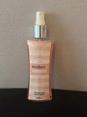 Madonna Exquisite Body Mist 100ml - Fräsch body mist från Madonna i doften Exquisite. Flaskan är 100 ml, har en elegant rosa och vit design med silvrig spraypump. Perfekt att spraya på kroppen för en lätt och uppfriskande doft. Flaskan är smal och lätt att ta med i väskan.