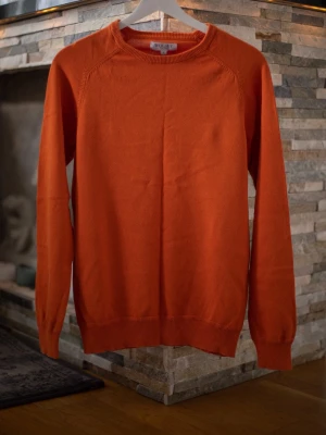 Orange stickad tröja från Wolsey - Snygg orange stickad tröja från Wolsey med rund halsringning och ribbade muddar vid ärmslut och nederkant. Enkel och stilren design som passar perfekt till lager-på-lager-look. Perfekt för dig som gillar färg och vill sticka ut.