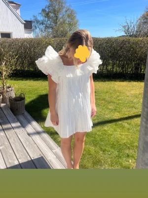 Vit plisserad klänning med volang - Superfin vit klänning med plisserat tyg och stora volangdetaljer vid axlarna från Zara. Klänningen har en lös passform och är ärmlös. Storlek M men passar också S och möjligtvis XS till längden. Mycket bra skick. Köpt på Vinted för 1700kr och har själv aldrig använt.