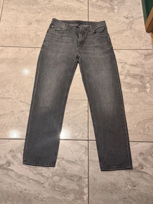 Gråa jeans från Tommy hilfiger  - Säljer ett par grå jeans från Tommy hilfiger. Jeansen har en snygg tvättad look, Perfekt för en avslappnad och lite mer lyxiga stilen. Jeansen är till människor som ligger på 164 i barn storlek. Hör av dig vid fler frågor!