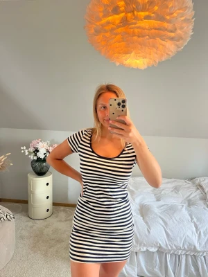 Randig kort klänning i bomull - Snygg kort klänning med marinblå och vita ränder. Modellen har rund halsringning och korta ärmar, perfekt för en avslappnad och trendig look. Tillverkad i mjuk bomull som känns skön mot huden.