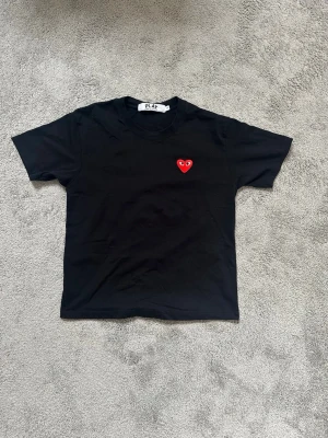 Svart Comme des Garçons PLAY t-shirt - Svart t-shirt från Comme des Garçons PLAY med det ikoniska röda hjärtat med ögon broderat på bröstet. Klassisk rund hals och korta ärmar. Tillverkad i mjuk bomull för en skön och stilren look.