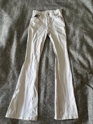 Vita bootcut jeans - Säljer ett par vita bootcut jeans och klassisk femficksdesign. Jeansen har vida ben och stängs med knapp och dragkedja. 