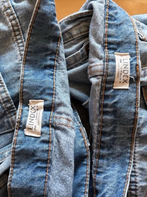 Ljusblå jeans från Lindex - Säljer ett par ljusblå jeans från Lindex med klassisk femficksdesign och raka ben. Jeansen har kontrastsömmar och är tillverkade i mjukt denimtyg. Perfekta för en avslappnad och trendig look.