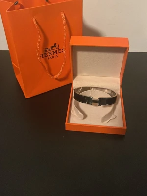 Svart H armband i metall - Snyggt svart armband från H i metall med den ikoniska H-detaljen framtill. Armbandet har en stilren och modern design med blanka svarta partier och silverfärgade detaljer. Perfekt accessoar för att lyfta din outfit.
