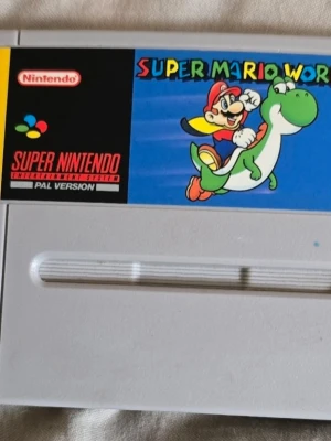 Super Mario World SNES spel - Klassiskt Super Mario World spel till Super Nintendo (SNES), PAL-version. Grå kassett med färgglad etikett där Mario rider på Yoshi. Perfekt för dig som gillar retrospel och vill återuppleva gamla favoriter.