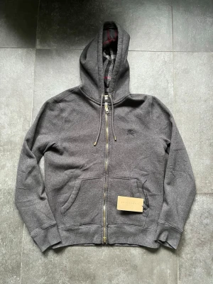 Burberry zip hoodie  - Tjena, säljer nu denna riktigt snygga och populära burberry zip hoodien, den är i mycket bra skick utan några skador, färgen är mörkgrå vilket är en av de populäraste och sällsyntaste färgerna, den är storlek S och den sitter bra på mig som är 180 cm och väger 65 kg, tagsen ingår och på den finns också äktehetsbeviset, hör av er vid frågor och funderingar🙌🤝 