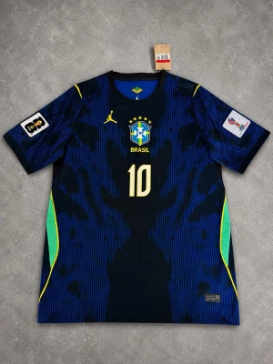 Blå Brasilien Neymar Jr matchtröja - Snygg blå matchtröja från Brasilien med Neymar Jr och nummer 10 på ryggen. Tröjan har gula och gröna detaljer, officiella loggor och patchar på ärmarna. Tillverkad i lätt och ventilerande material, perfekt för fotboll eller träning.