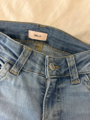 Ljusblå ripped jeans från Nelly - Säljer ett par ljusblå jeans från Nelly med snygga slitningar på benen. Jeansen har klassisk femficksmodell, bälteshällor och knappstängning. Perfekta för en trendig och avslappnad look.