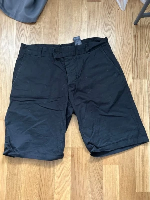 Svarta shorts från H&M - Klassiska svarta shorts från H&M med normal passform och bälteshällor. Tillverkade i bomull, perfekta för varma dagar. Enkla att matcha med olika stilar och har fickor på sidorna.