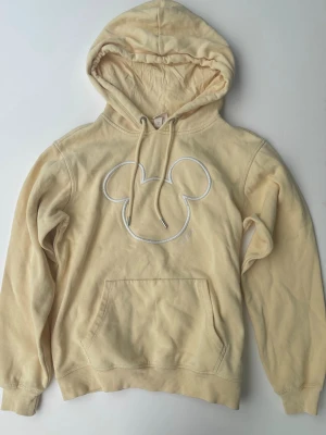 Gul hoodie med Musse Pigg från H&M - Snygg ljusgul hoodie från H&M med broderad Musse Pigg-siluett på bröstet. Tillverkad i mjuk bomull för skön känsla.