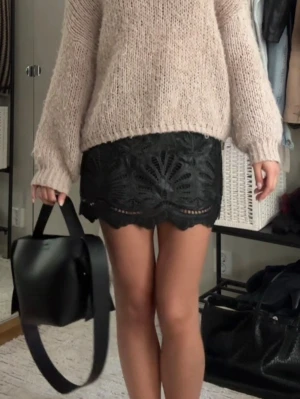 Svart spetskjol med volangkant - Snygg svart kortkjol i spets med dekorativt broderat mönster och vågig volangkant. Kjolen har en feminin och trendig look som passar perfekt till en stickad tröja eller crop top. Ingen synlig dragkedja eller knappar.