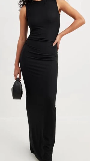 Svart långklänning med slits - Stilren svart långklänning i figurnära modell med ärmlös design och rund halsringning. Klänningen har en diskret slits på sidan för extra rörelsefrihet. Perfekt för dig som gillar en klassisk och elegant look.