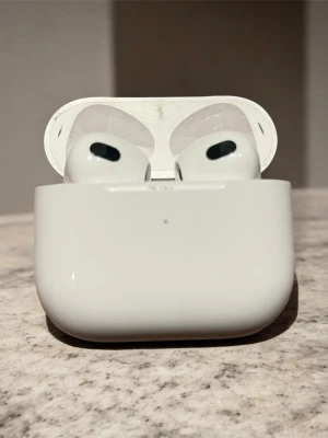Apple AirPods 3 med laddningsetui - Säljer ett par Apple AirPods 3 med vitt, blankt laddningsetui. Perfekt för trådlös musik och samtal, lätt att ta med överallt.
