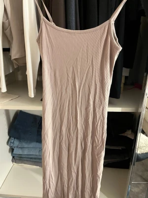Beige ribbad långklänning Amisu - Säljer en beige ribbad långklänning från Amisu i storlek 34. Klänningen har smala axelband och är figurnära med en enkel, stilren design. Perfekt för sommardagar eller när du vill ha en avslappnad men snygg look.