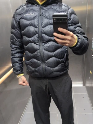 Mörkblå dunjacka från Peak Performance - Snygg mörkblå dunjacka från Peak Performance med quiltad design och dragkedja framtill. Jackan har huva och logga på bröstet. Perfekt för kalla dagar när du vill hålla värmen och ändå se stilren ut. Helt ny oanvänd nypris 2999 säljes för 1500 äkta som sagt tio av tio oanvänd. Passar smal 