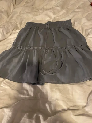 Grå volangkjol från SHEIN - Supersöt grå kortkjol från SHEIN med volangdetaljer och bred resår i midjan. Kjolen har ett tunt, flowy material och knytband i midjan för extra stilpoäng. Perfekt för dig som gillar en feminin och trendig look.