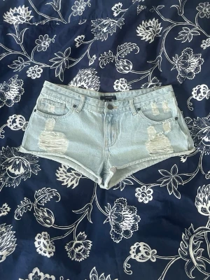 Ljusblå denimshorts med slitningar - Säljer ett par ljusblå denimshorts med råa kanter och slitna detaljer framtill. Klassisk femficksmodell med knapp och dragkedja. Säljer eftersom de är inte rätt storlek för mig.🤍