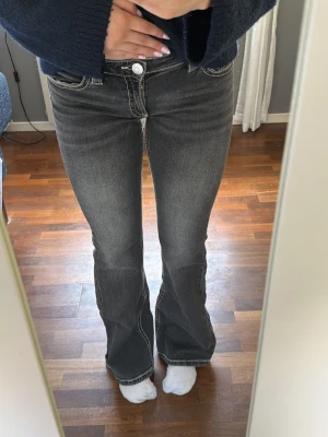 Grå bootcut jeans med kontrastsömmar - Säljer ett par grå bootcut jeans med vita kontrastsömmar och snygga detaljer på bakfickorna. Jeansen har låg midja och använda fåtal gånger. Säljer då jeansen inte kommer till användning längre. Och jag är 169cm lång💕