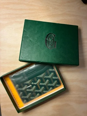 Grön korthållare - Snygg grön korthållare  med det klassiska mönstret i vitt och grått. Tillverkad i canvas med läderdetaljer och levereras i ask. Perfekt för dig som vill ha en exklusiv och stilren accessoar till dina kort.