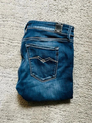 Replay jeans - Säljer ett par blå jeans från Replay med klassisk femficksdesign och snygga slitningar. Jeansen har en cool detalj på bakfickan och är tillverkade i stretchigt denim för skön passform. Perfekta till sneakers eller boots!