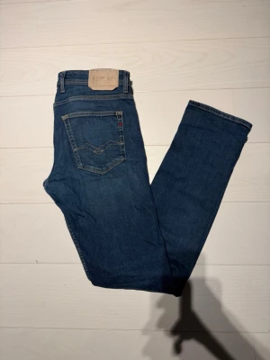 Blå jeans från Replay - Säljer ett par klassiska blå jeans från Replay med fem fickor och raka ben. Jeansen har snygga kontrastsömmar och en patch med Replay-loggan bak i midjan. Perfekta för en avslappnad och trendig look.