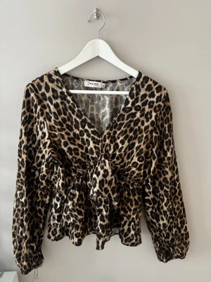 Leopardmönstrad blus med knyt - Trendig leopardmönstrad blus från Youlime med v-ringning och knyt i midjan. Blusen har långa ärmar med resår vid ärmslut och är tillverkad i ett lätt, mjukt tyg som ger en snygg siluett. Perfekt för dig som vill sticka ut med ett djurmönster. Den har ett hål vid ena armen längst ner men superlätt att sy ihop! Skulle säga att den passar xs/s och inte m/l som det står på tröjan. 