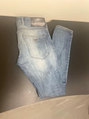 Blå jeans från Emporio Armani - Snygga blå jeans från Emporio Armani med ljus tvätt och raka ben. Jeansen har klassiska fem fickor, synliga sömmar och en diskret logga på bakfickan. Tillverkade i denim med en cool vintagekänsla och detaljerade fickor framtill.