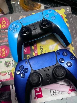 2 ps5 kontroller för 500kr - Två PlayStation 5 DualSense handkontroller i olika blå nyanser. En är ljusblå och den andra är metallicblå, båda med svarta detaljer och klassisk ergonomisk form. Tillverkade i plast med greppvänlig design och ikoniska PlayStation-knappar.