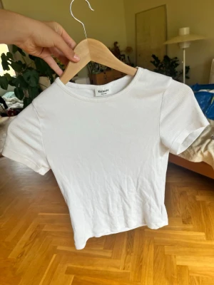 Vit ribbad t-shirt från Kappahl - En basic vit ribbad t-shirt från Kappahl i storlek 158/164. T-shirten har korta ärmar, rund halsringning och är gjord i mjuk bomull. Perfekt att matcha med jeans eller kjol för en clean och enkel look.