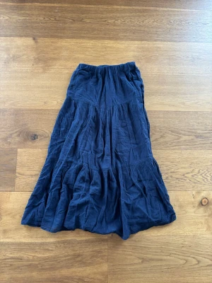 Mörkblå långkjol från Gina Tricot - Säljer en mörkblå långkjol från Gina Tricot i luftig bomull. Kjolen har resår i midjan och flera volanger som ger ett snyggt fall. Perfekt för dig som gillar en avslappnad och trendig stil.