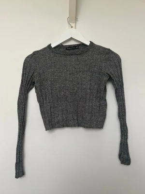 Mörkgrå  ribbstickad croptröja Bershka - Mörkgrå ribbad långärmad croptröja. Inköpt på Plick ursprungligen ifrån Bershka. Använd och i fint skick. Storlek XS. 