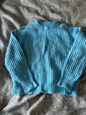 Blå ribbstickad tröja - Säljer en blå ribbstickad tröja med rund hals och långa ärmar. Tröjan har en avslappnad passform och breda muddar vid ärmslut och nederkant. Perfekt för dig som gillar en enkel men snygg look.
