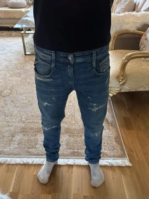 Blå slim fit jeans med slitningar - Säljer ett par blå slim fit jeans med snygga slitningar och tvättade detaljer framtill. Jeansen har fem fickor, normal midja och klassisk knappgylf. Materialet är stretchigt denim som sitter tajt längs benen. Perfekta för dig som gillar en trendig och avslappnad look. Pris kan diskuteras.