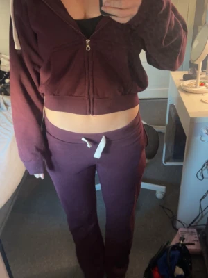 Vinrött mjukis sett  med dragsko - Säljer ett vinrött mjukissett med vit dragsko i midjan och fickor bak. Byxorna har en relaxed fit och är gjorda i mjukt, bekvämt material som passar perfekt för chill dagar. Snygg detalj med broderad söm på bakfickan.