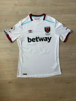 Vit Fotbollströja West Ham United Bortatröja 2016/17 Storlek L - Mycket fin fotbollströja i vit färg. Tröjan är i mycket bra skick och sparsamt använda. |  Äkta som allt annat jag säljer! ✅ |  Storlek: L | Skick: Mycket Bra Skick - Tyvärr har trycket blivit lite missfärgat på sponsortexten (SE SISTA BILD) | Färg: Vit | Märke: Umbro | Modell: Fotbollströja |   Hör gärna av dig vid frågor så svarar jag så fort jag kan! 😁